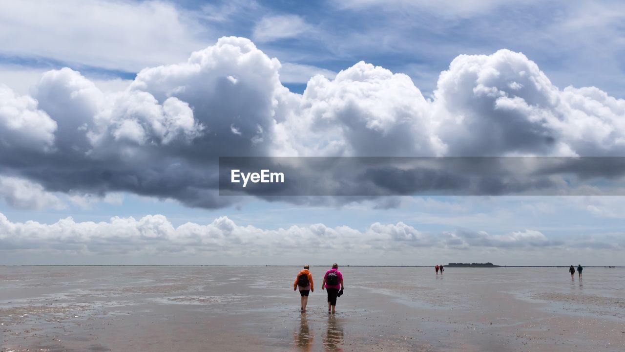 Rear view of people at beach against cloudy sky