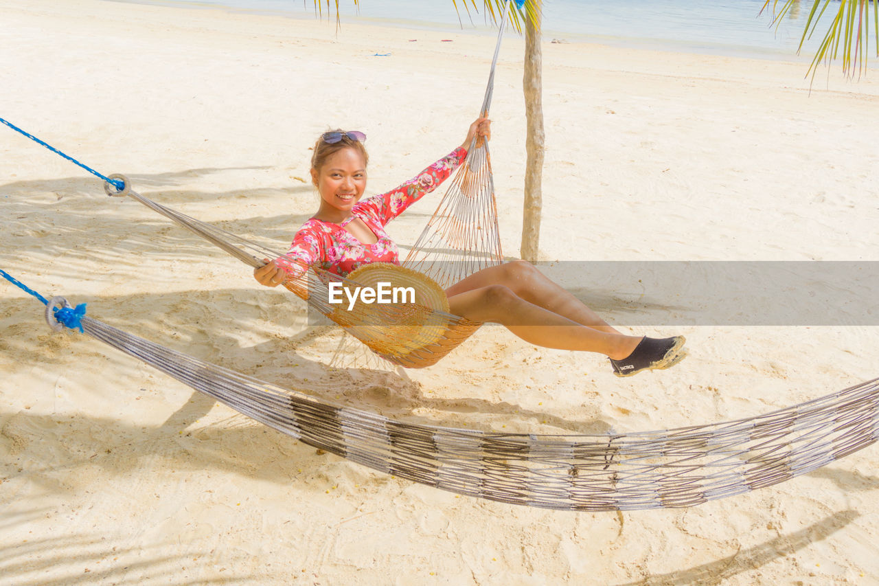 Smiling woman sitting on hammock at beach