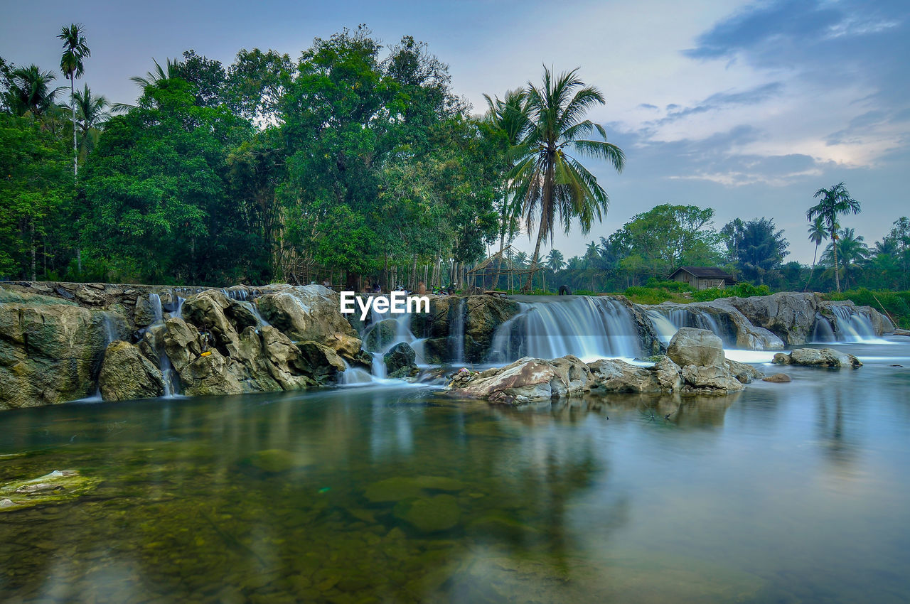 Scenic view of waterfall in forest against sky