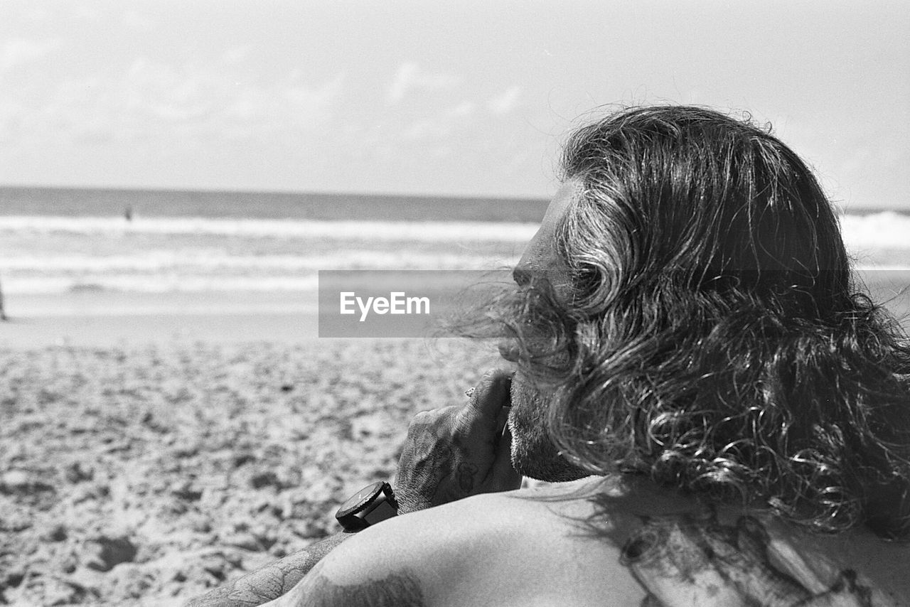 Rear view of man sitting at beach against sky