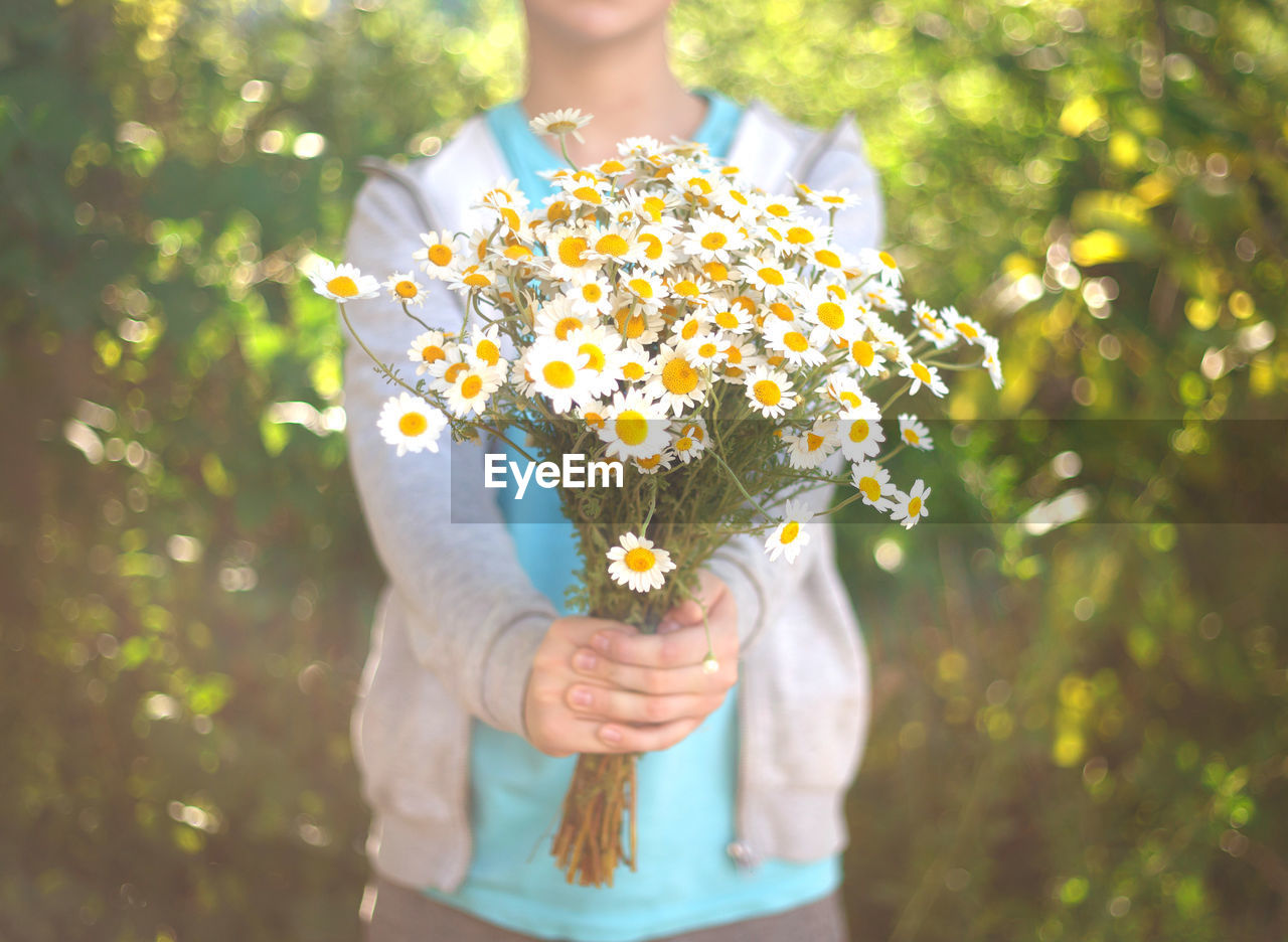 MIDSECTION OF PERSON HOLDING BOUQUET AGAINST YELLOW FLOWERING PLANT