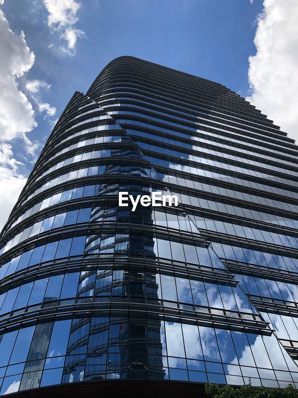 LOW ANGLE VIEW OF MODERN GLASS BUILDING AGAINST CLOUDY SKY