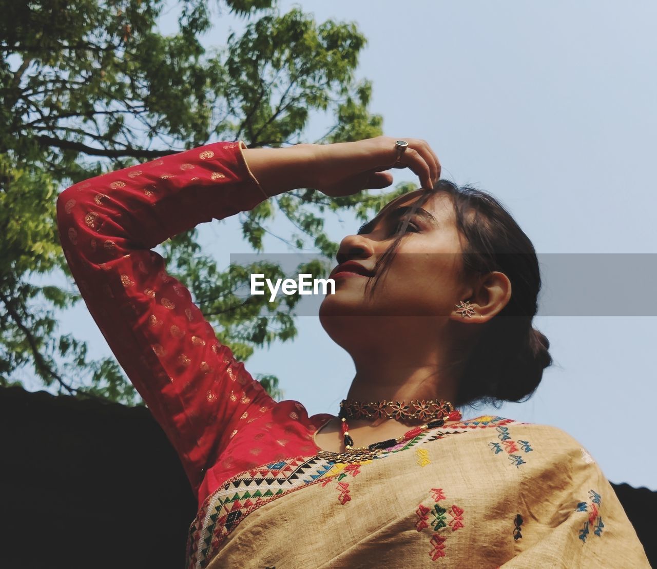 Side view of woman with arms crossed standing against sky