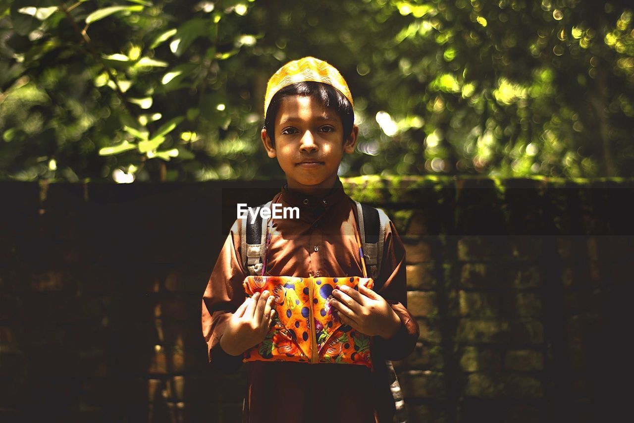 Portrait of boy holding koran against brick wall