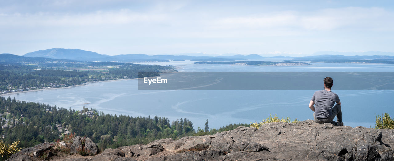 Young man enjoying panoramic view on island and surrounding ocean, vancouver island, bc, canada