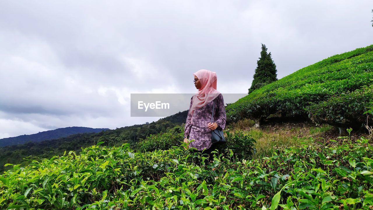 Woman standing by plants on land against sky