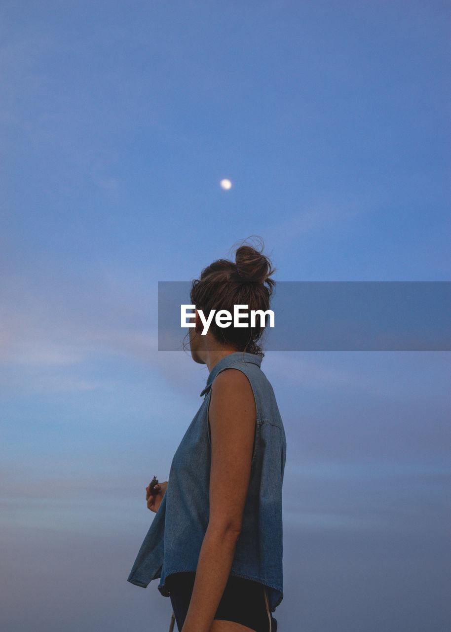 Side view of woman standing against sky during dusk