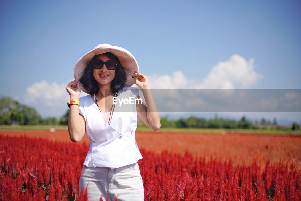 Smiling woman standing on field against sky