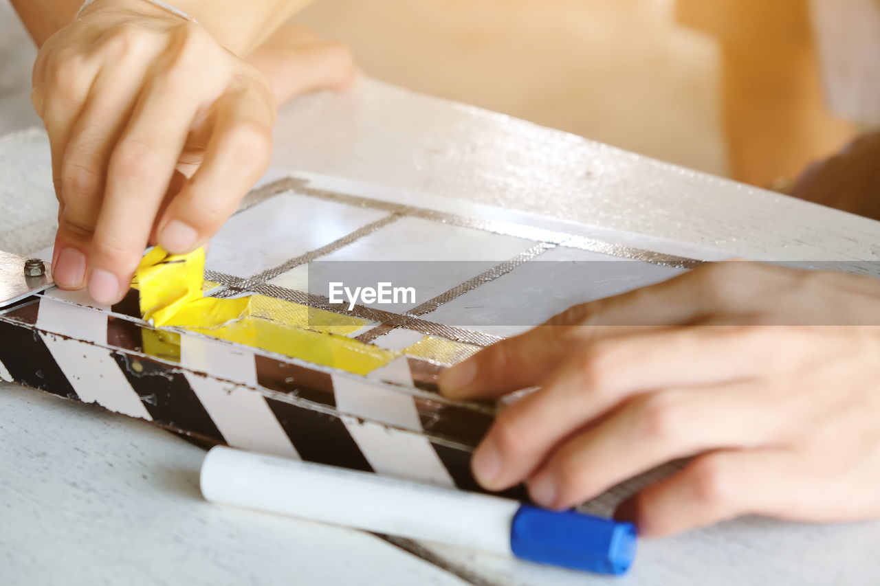 Close-up of cropped hands removing yellow tape from film slate