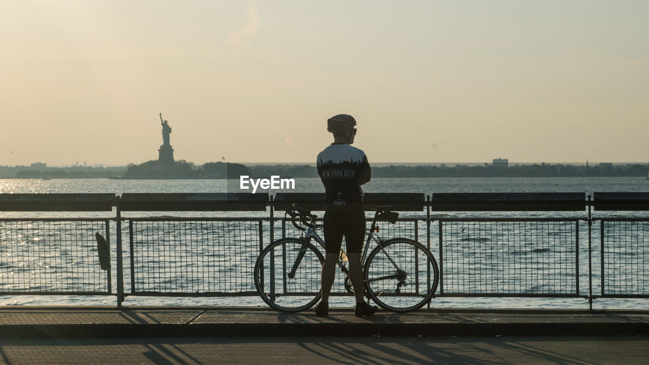 REAR VIEW OF MAN WITH BICYCLE STANDING ON RAILING