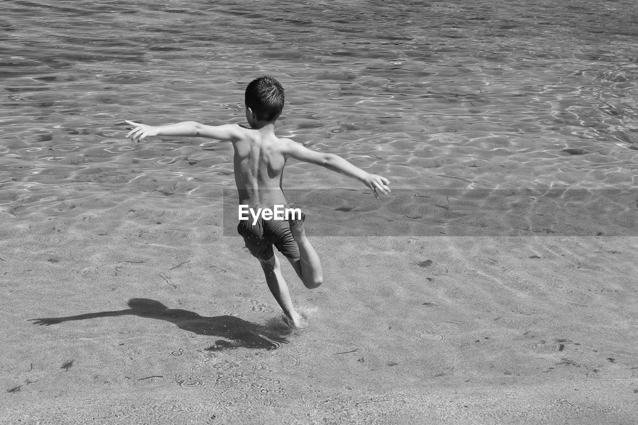 Rear view of shirtless boy running at beach