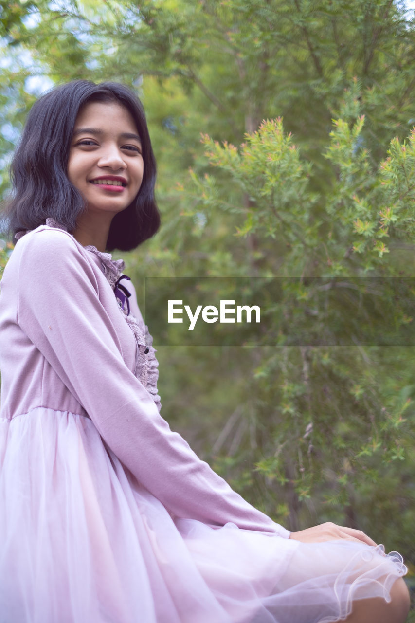 Portrait of smiling girl sitting against tree outdoors