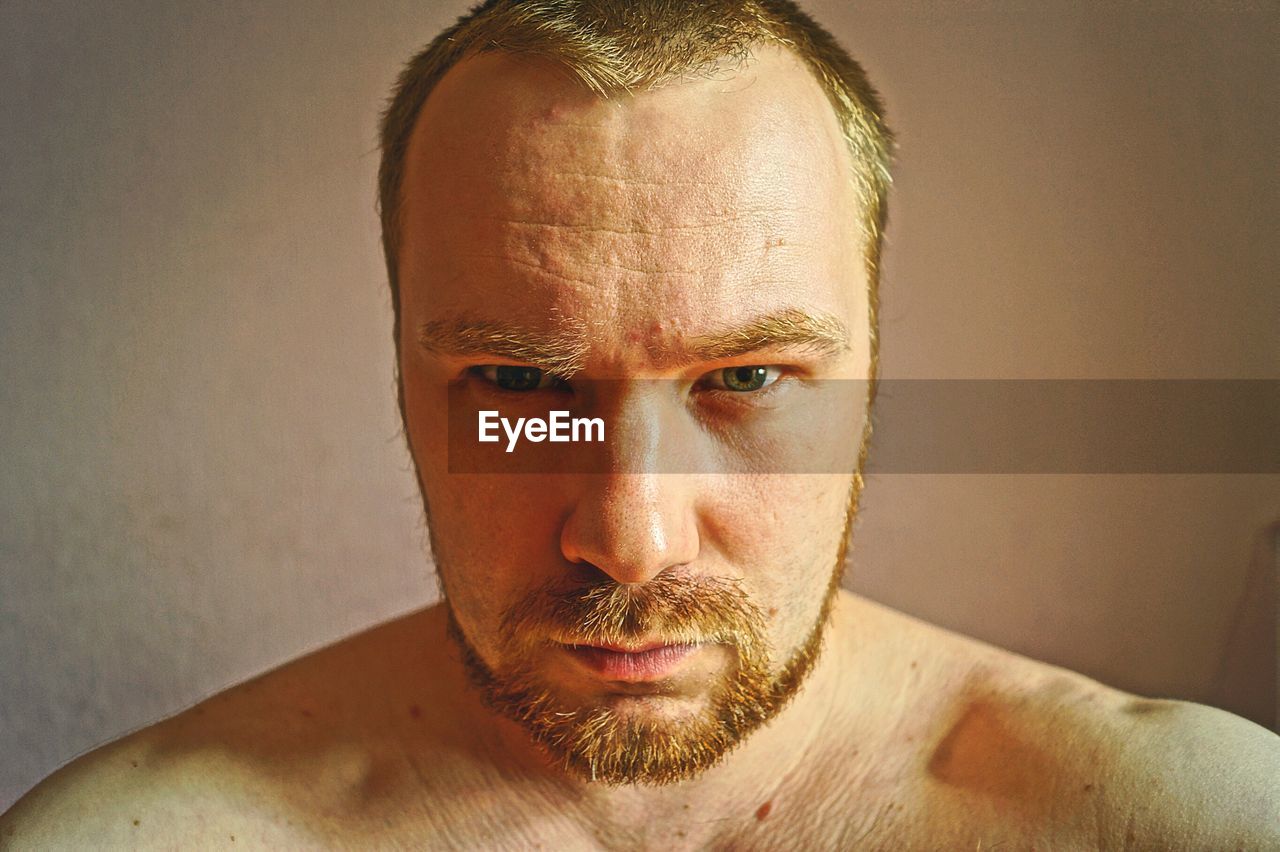 Close-up portrait of shirtless man against wall at home