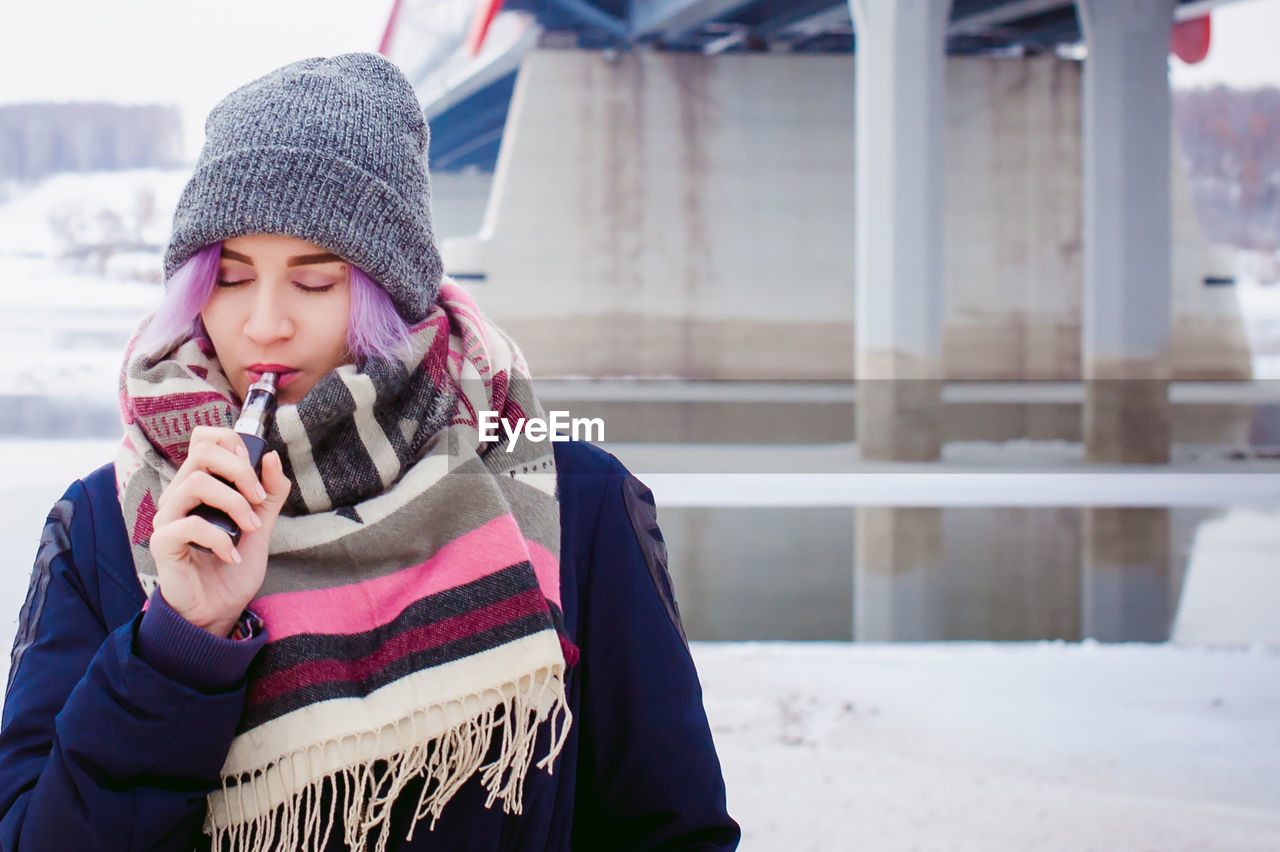 Young woman smoking electronic cigarette during winter