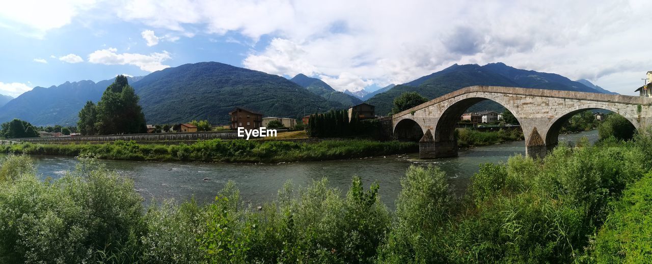 ARCH BRIDGE OVER RIVER BY MOUNTAINS AGAINST SKY