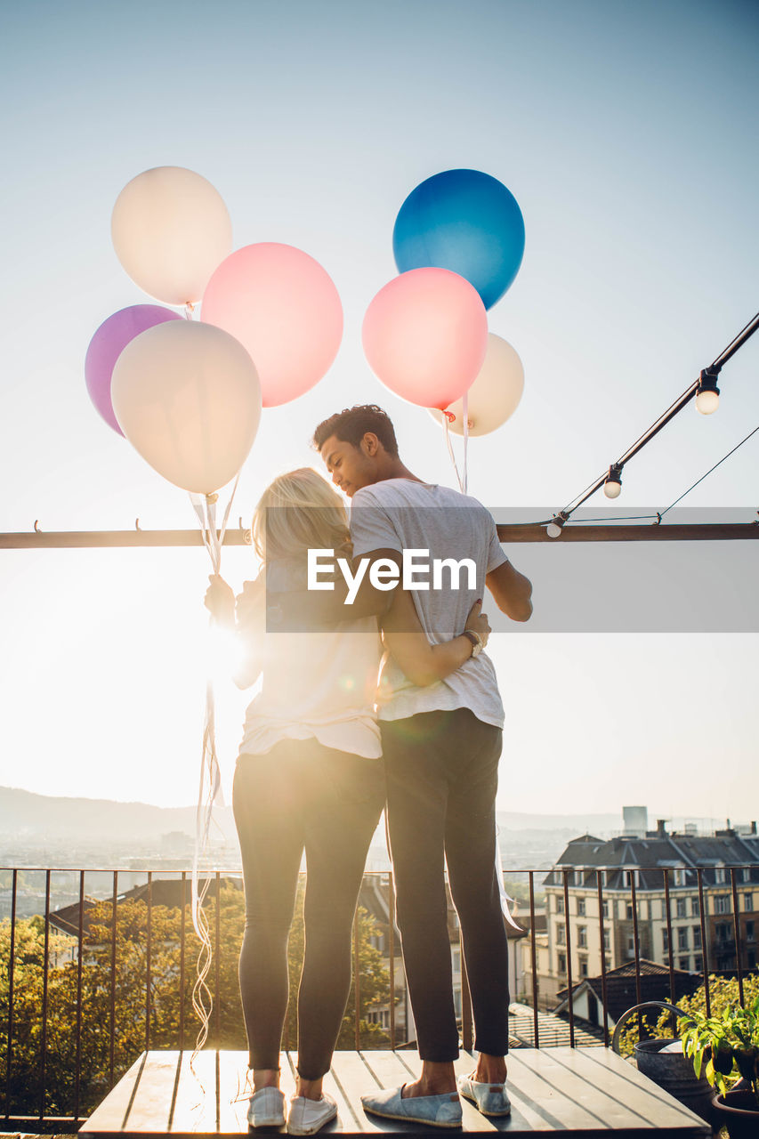 Rear view of couple standing with balloons against sky