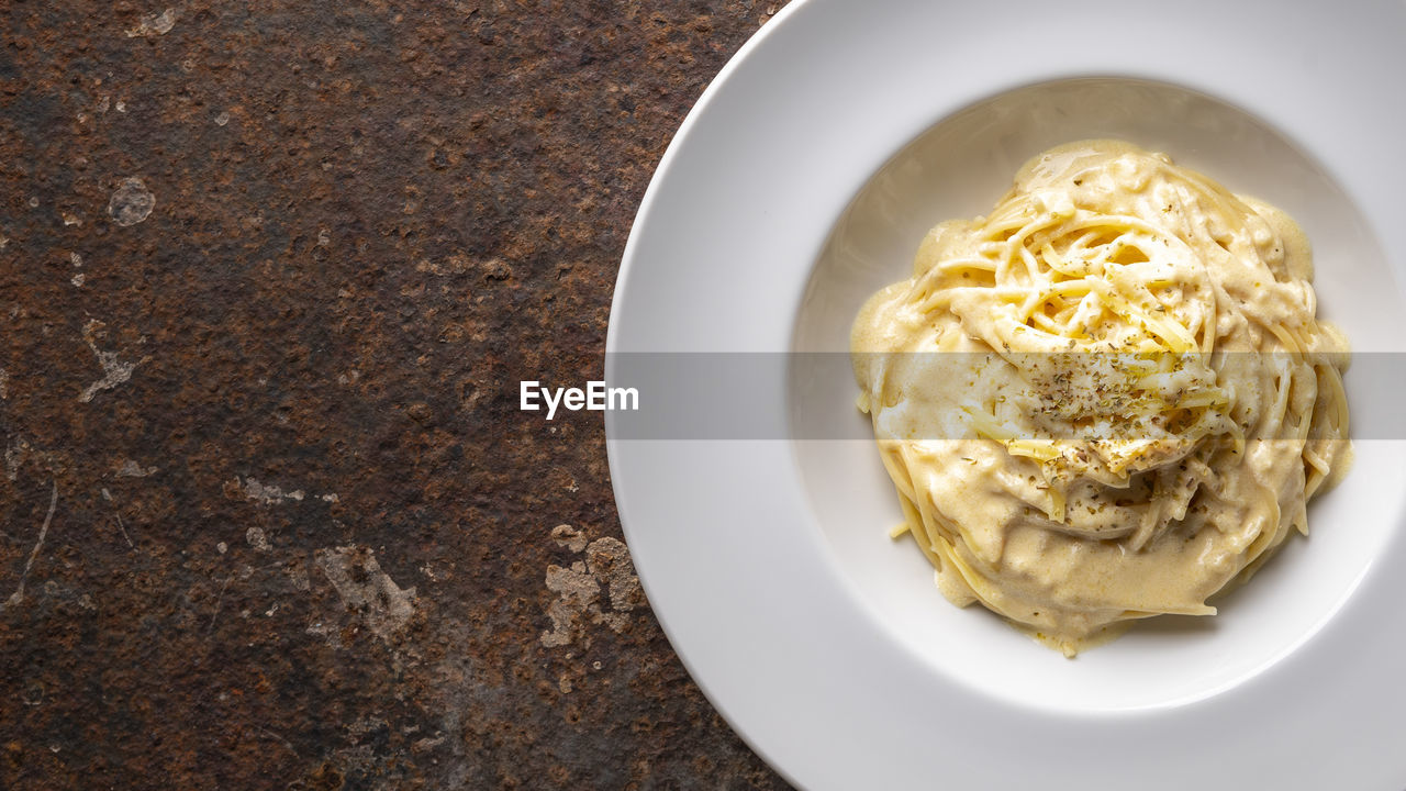 Spaghetti carbonara with cream sauce in ceramic plate on rusty texture background, copy space