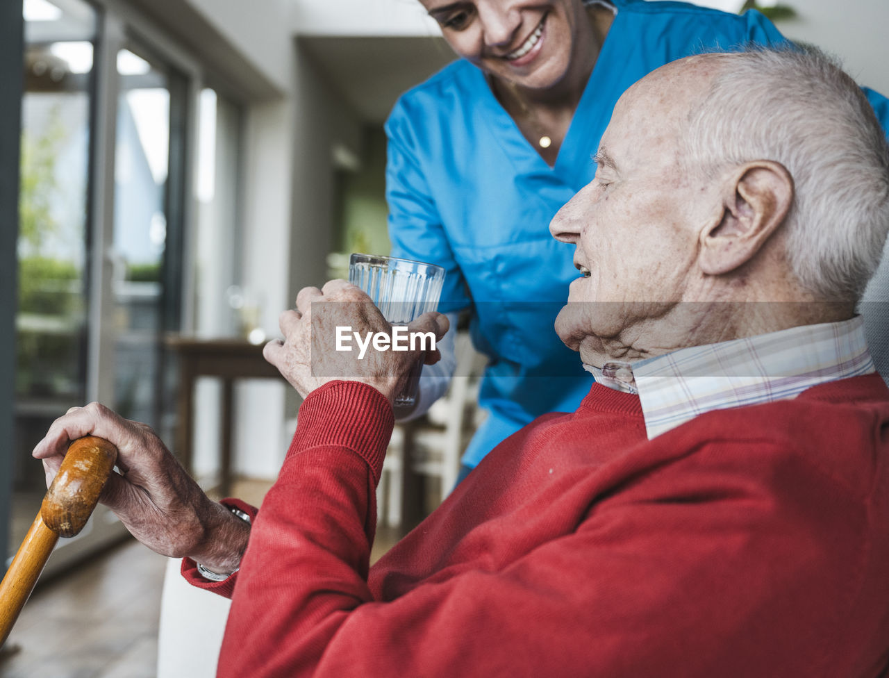 Smiling nurse giving water to senior man at home