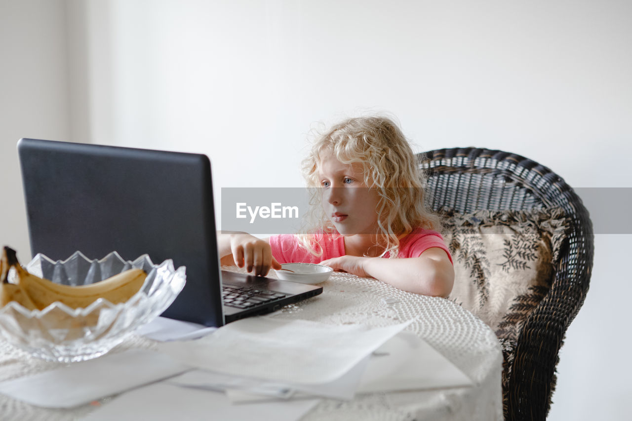 Young girl eating food and watching cartoons on laptop. child with digital gadget during meal. 