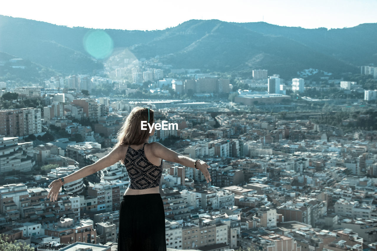 Woman standing with arms outstretched by cityscape and mountains