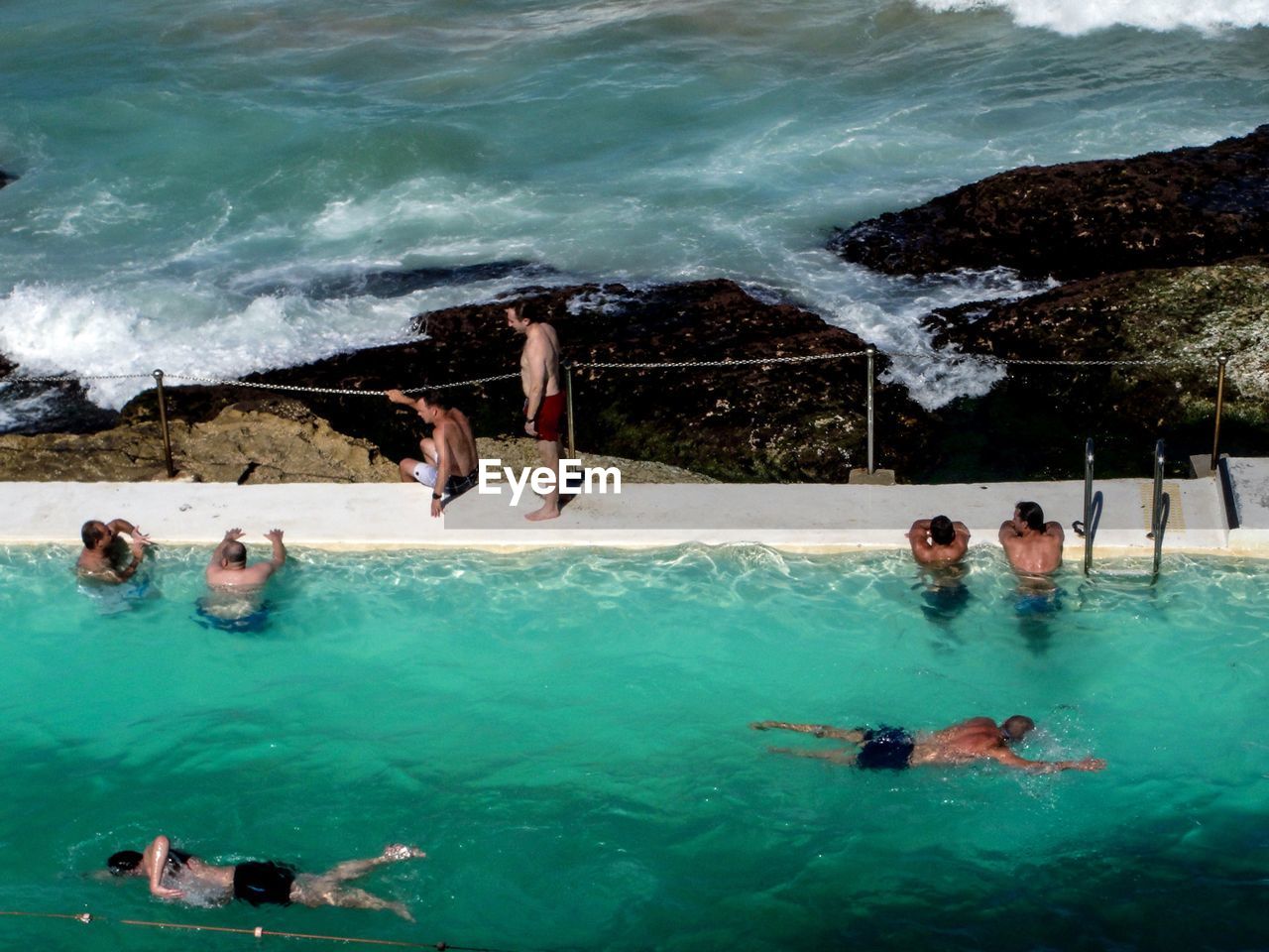 People in swimming pool against calm sea