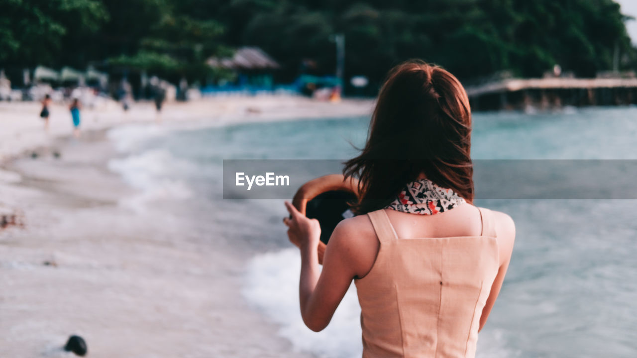 REAR VIEW OF WOMAN STANDING IN WATER AT BEACH