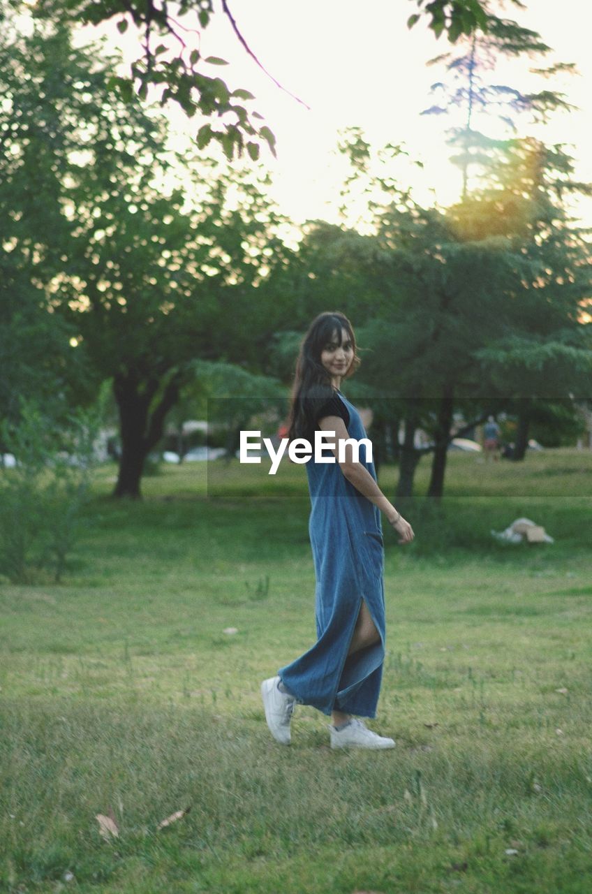 Portrait of young woman standing against trees at park