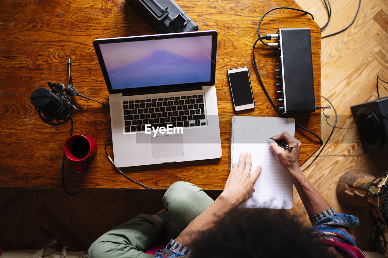 Male afro musician writing notes by laptop on table at home