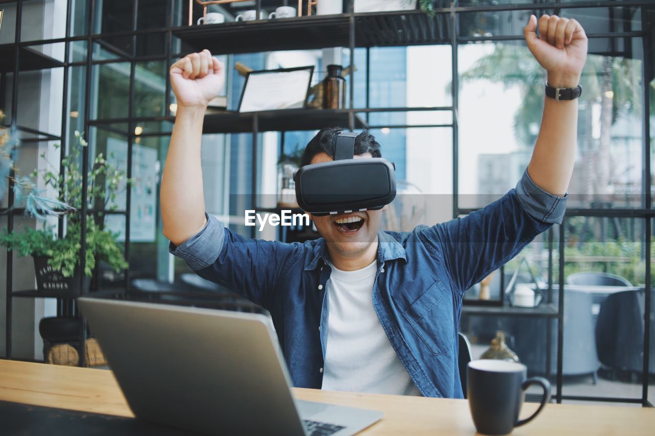 Smiling man gesturing while using virtual reality simulator at cafe