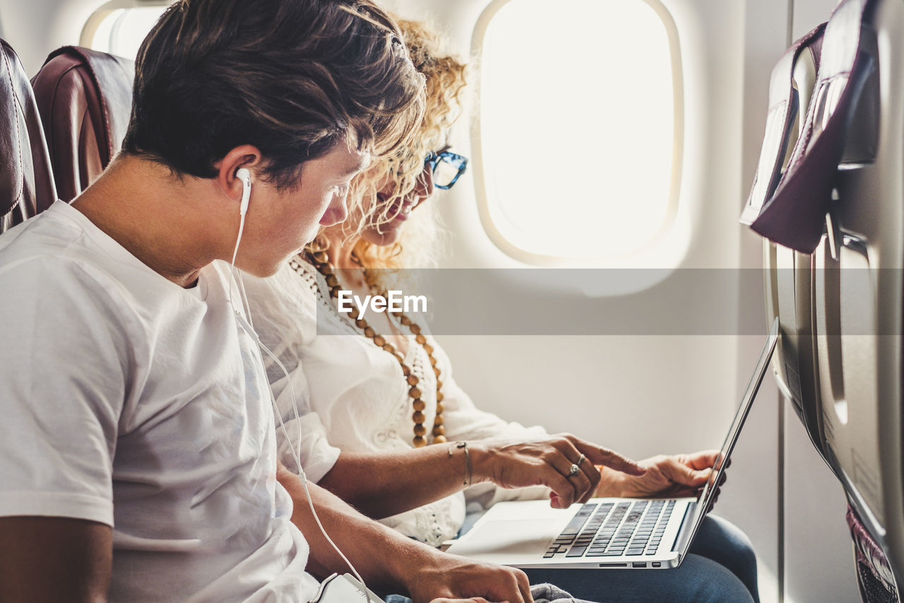 Man and woman using laptop while sitting in airplane