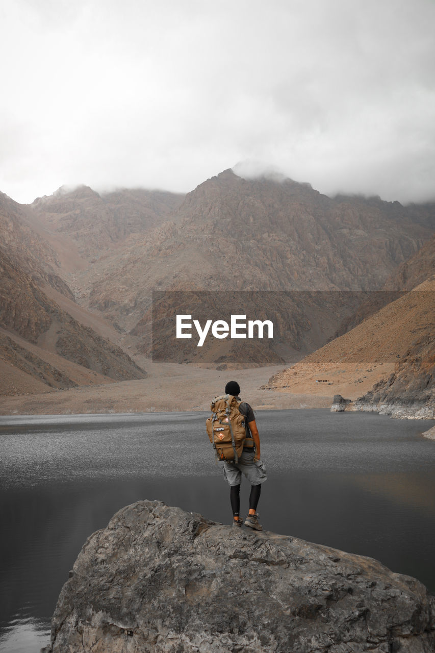 Rear view of man standing on rock by mountain against sky