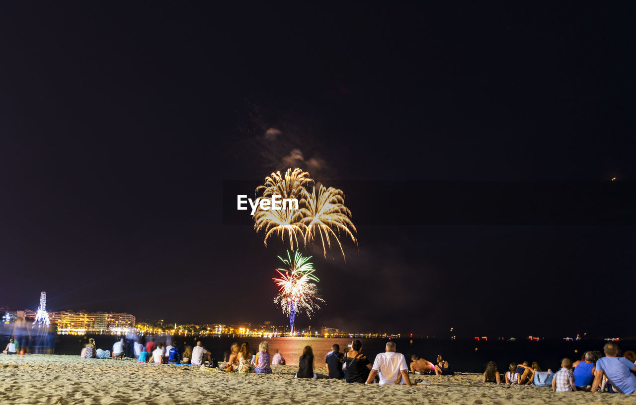 People watching firework display at beach against sky at night