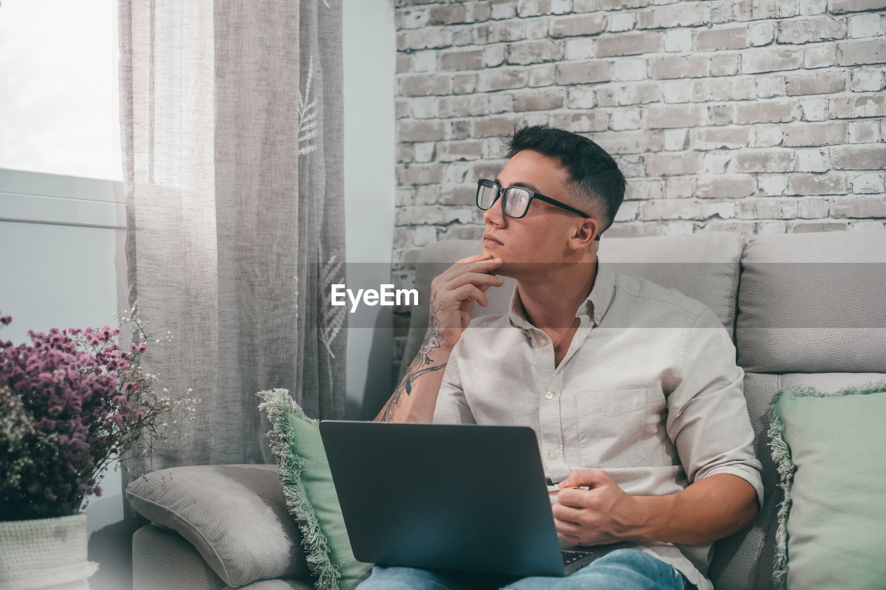 young man using laptop while sitting on sofa at home