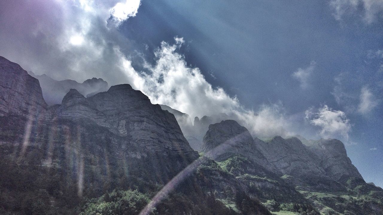 Low angle view of rocky mountains against cloudy sky