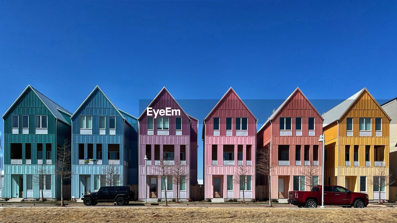 architecture, built structure, building exterior, building, house, residential district, sky, in a row, blue, beach, nature, row house, beach hut, no people, land, side by side, home, hut, residential area, clear sky, facade, home ownership, multi colored, city, day, outdoors, window, sand, town, estate, wood, mansion, copy space