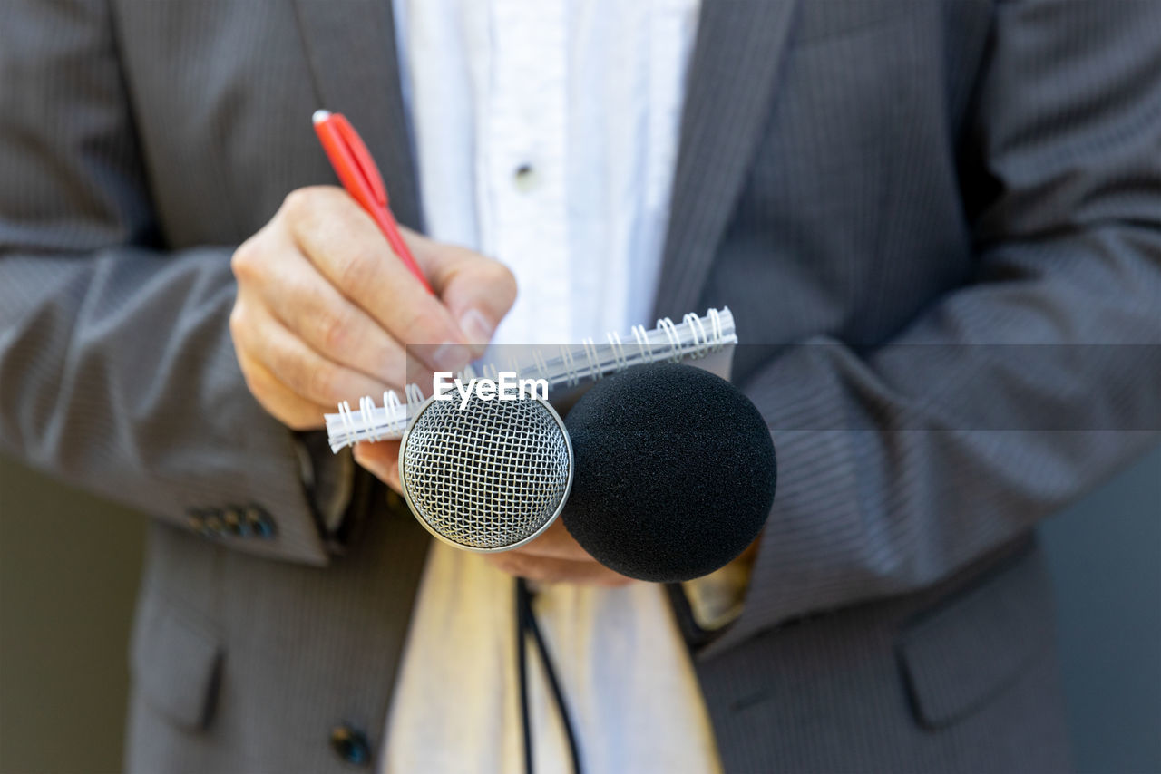 Correspondent or reporter at media event, holding microphone, writing notes. journalism concept.