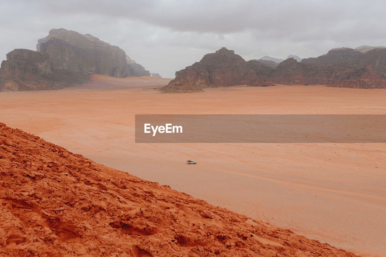 Scenic view of automobile riding in sandstone valley in wadi rum on cloudy day