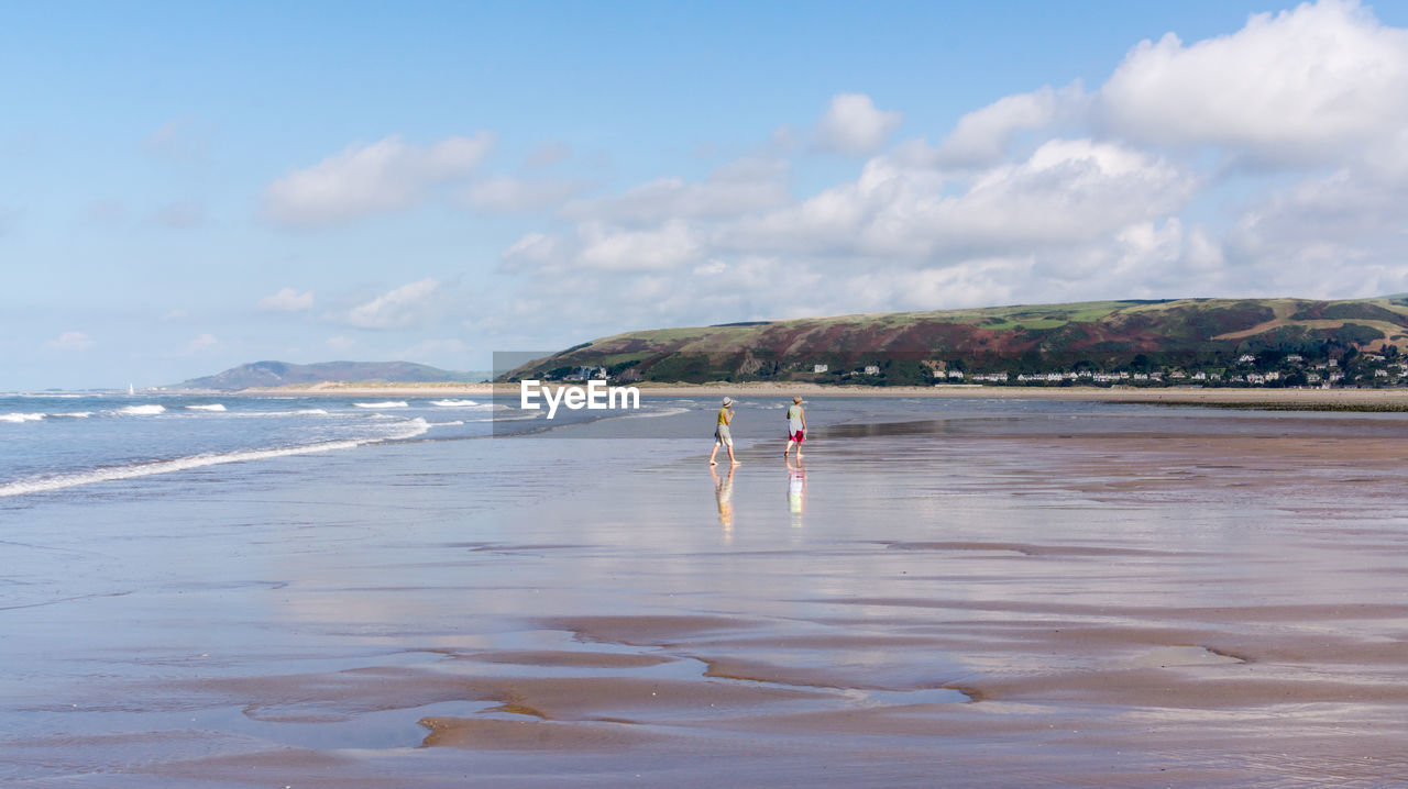 People walking at beach against sky