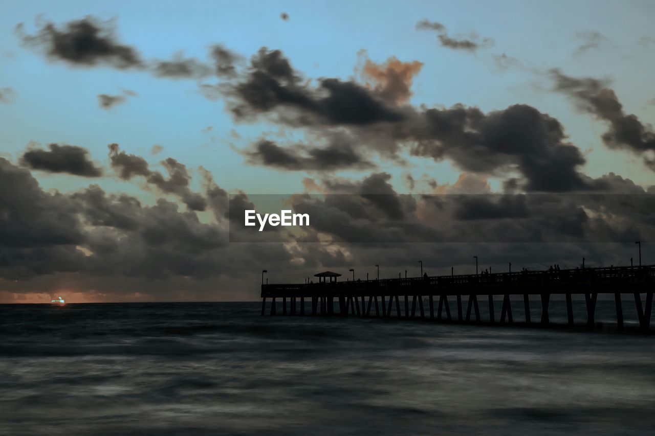 Silhouette pier over sea against cloudy sky during sunset