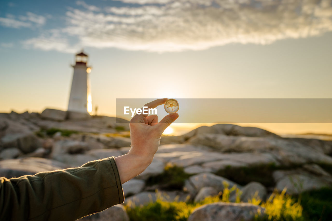 Person holding marble against sky during sunset