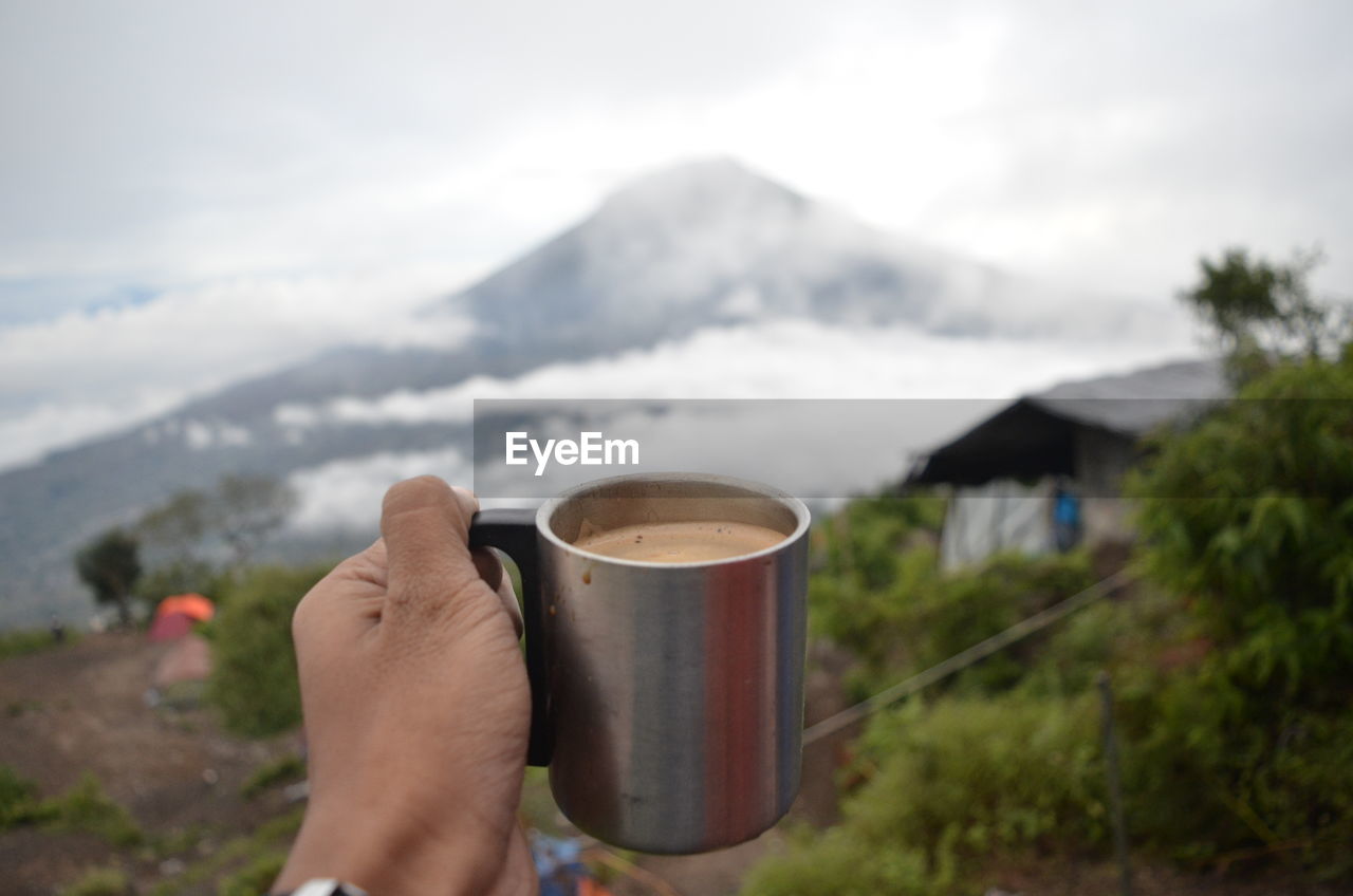 PERSON HOLDING COFFEE CUP AGAINST MOUNTAINS