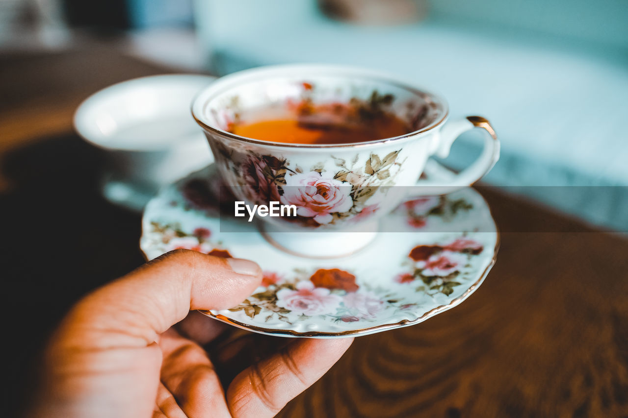 Close-up of hand holding tea cup over table