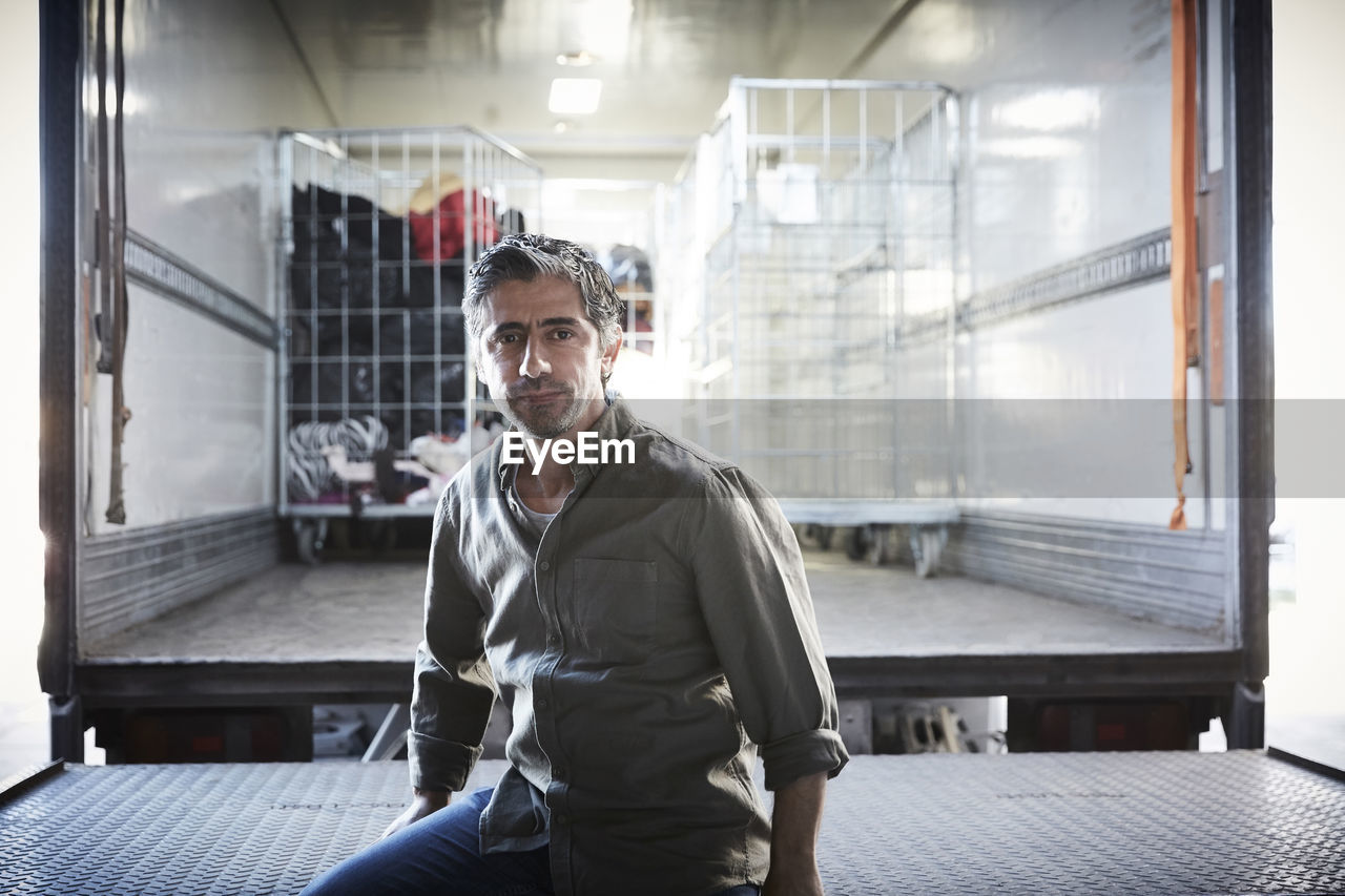 Portrait of mature male volunteer sitting against semi-truck at warehouse