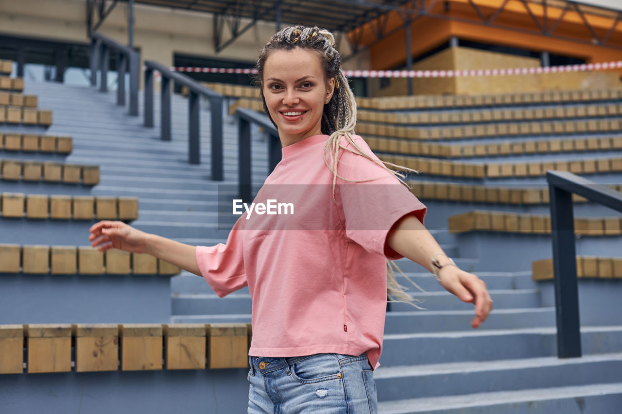 PORTRAIT OF HAPPY WOMAN STANDING AGAINST RAILING