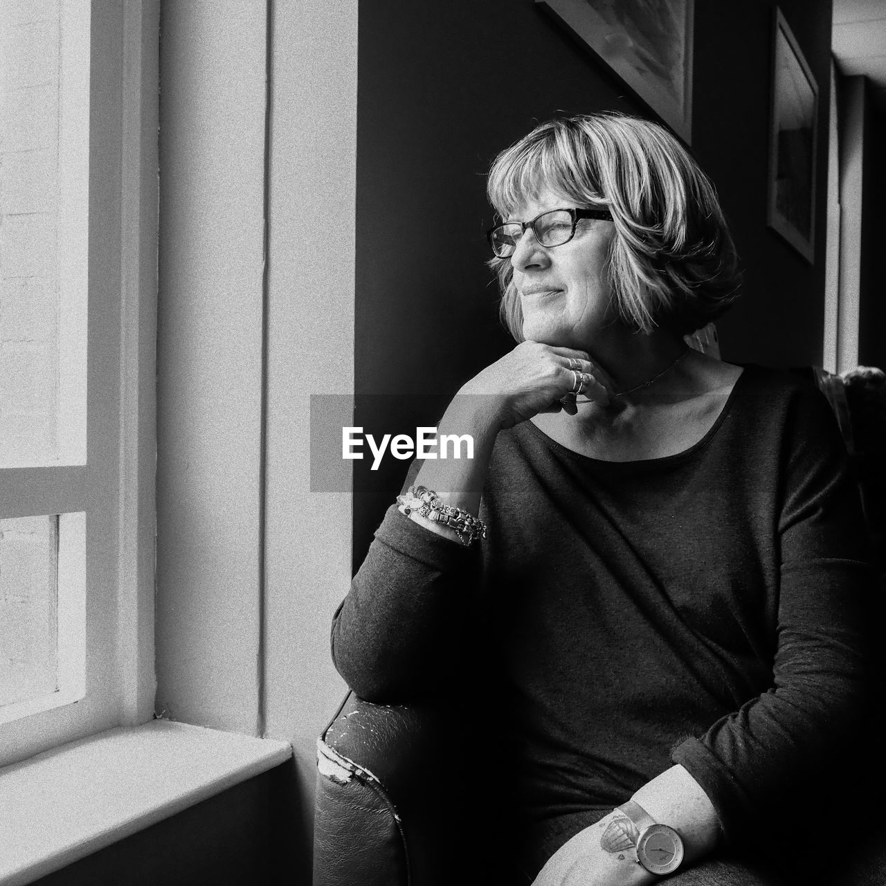 Thoughtful woman looking through window while sitting on chair at home