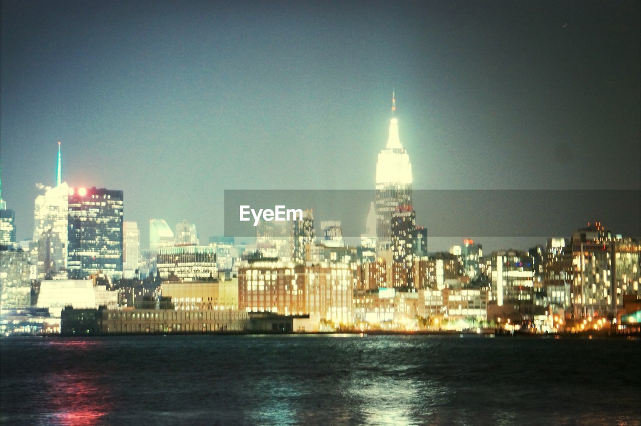 River in front of illuminated empire state building in city at night