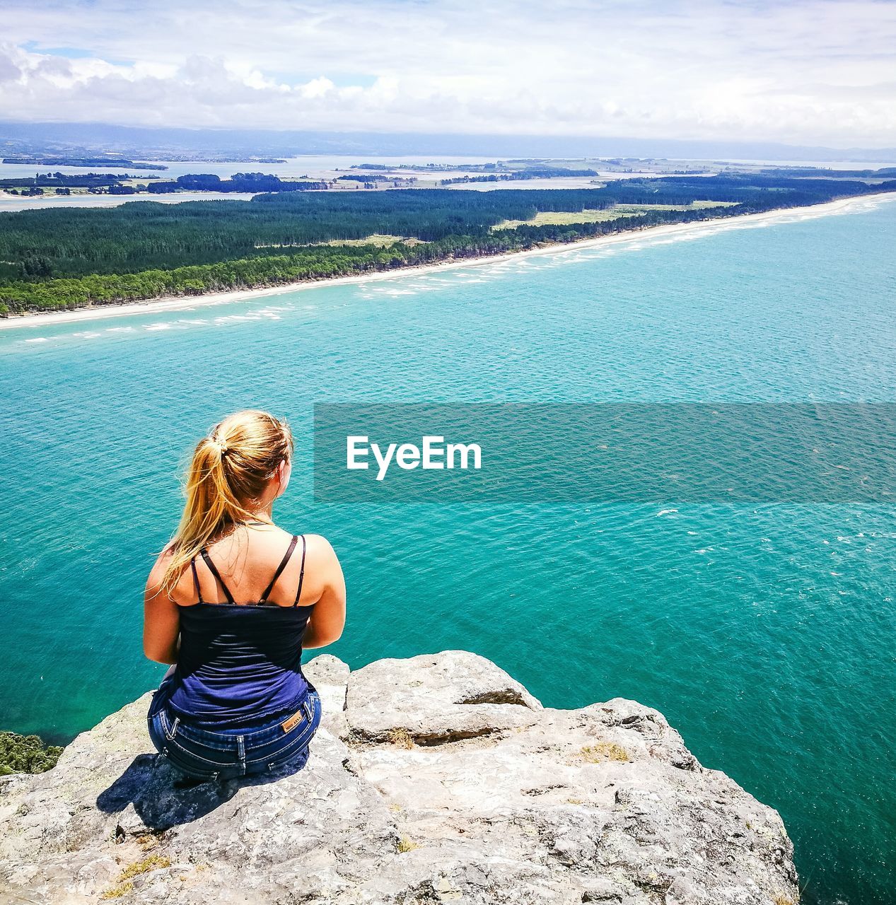 Rear view of woman sitting on rock by sea