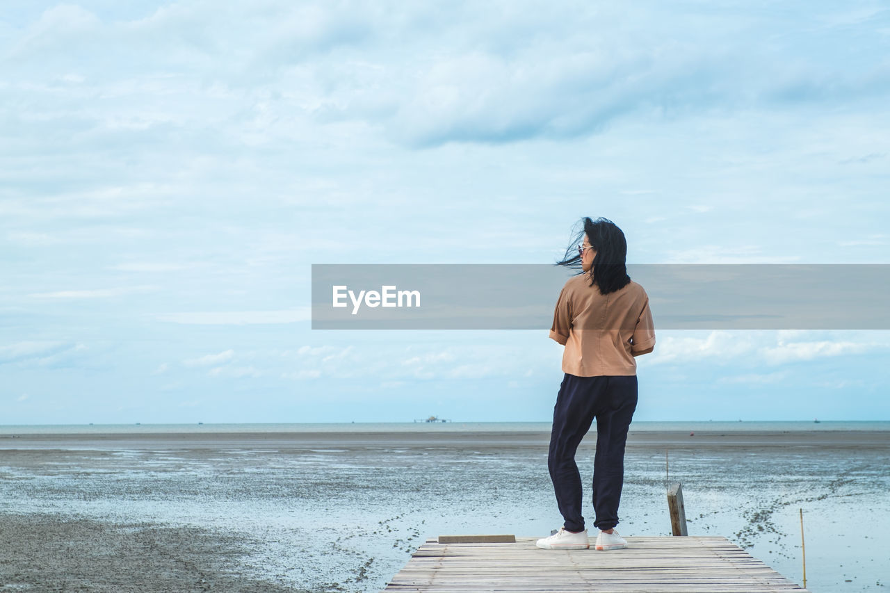 Woman standing on pier over sea against sky