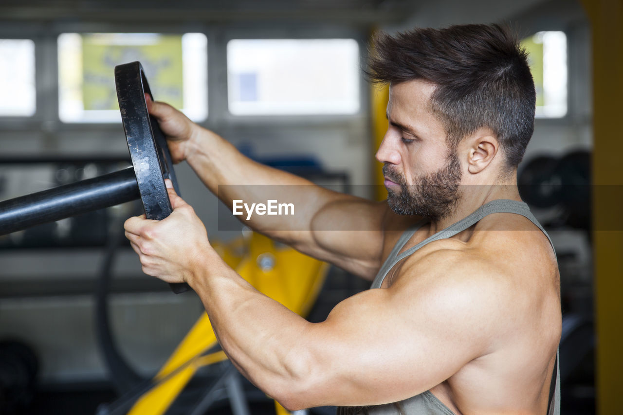 Close-up of muscular man holding dumbbell at gym