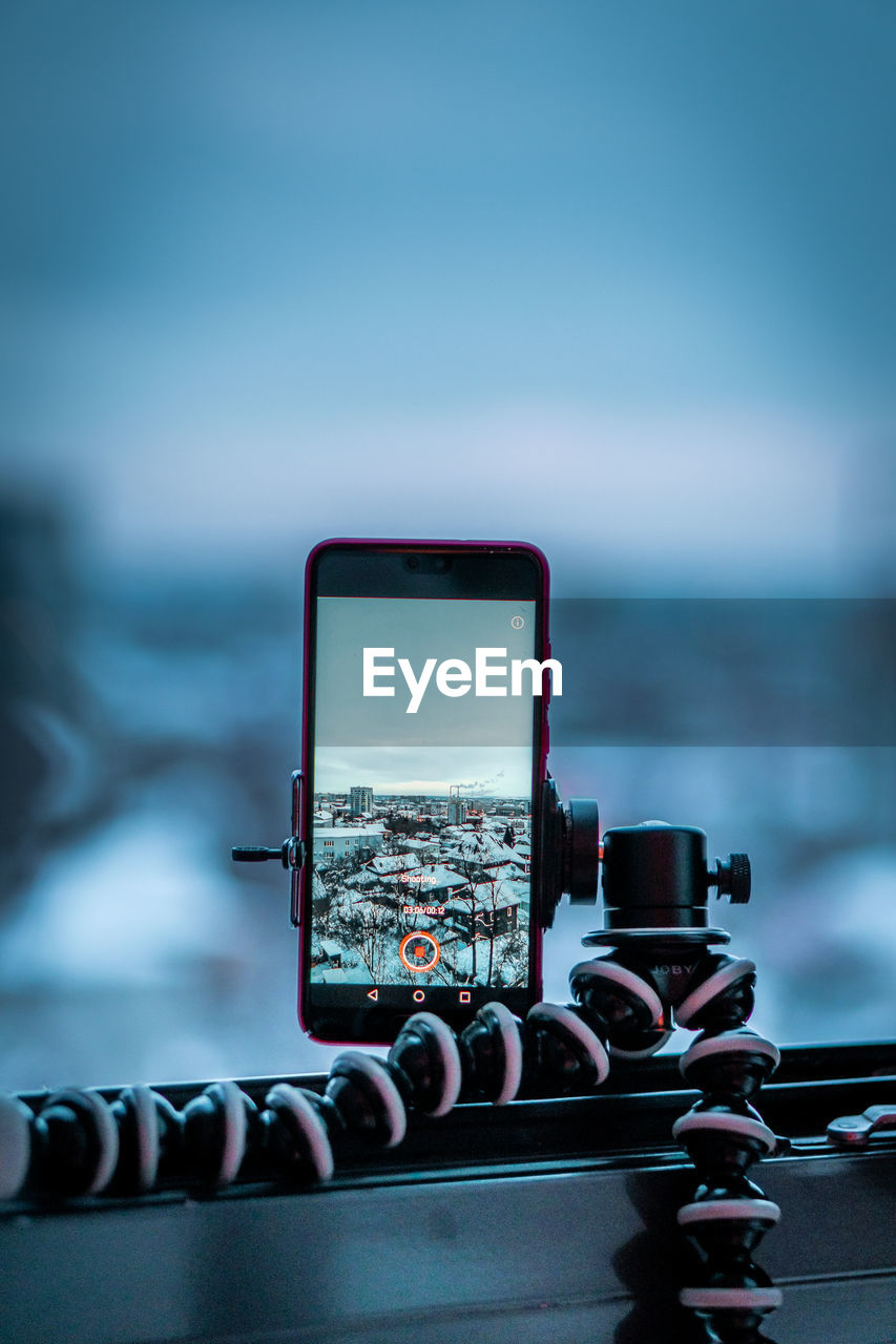 Close-up of mobile phone on railing against sky